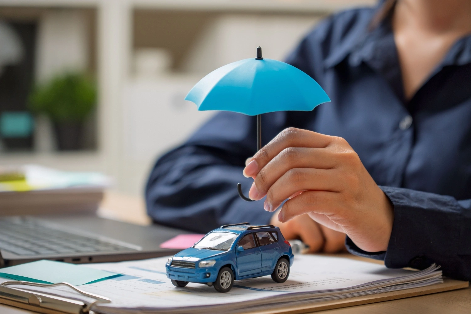 persona tiene ombrello in miniatura sopra modellino automobile, immagine che richiama concetto di assicurazione auto a noleggio